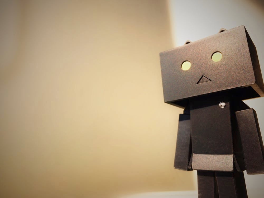 "Cardboard robot figure with glowing eyes, standing against a softly lit background, depicting creativity in toy design."