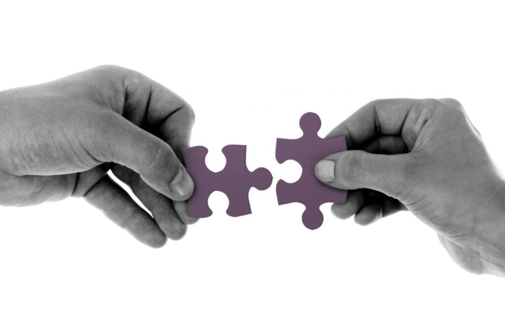 "Two hands connecting purple puzzle pieces, symbolizing teamwork and collaboration for problem-solving initiatives."