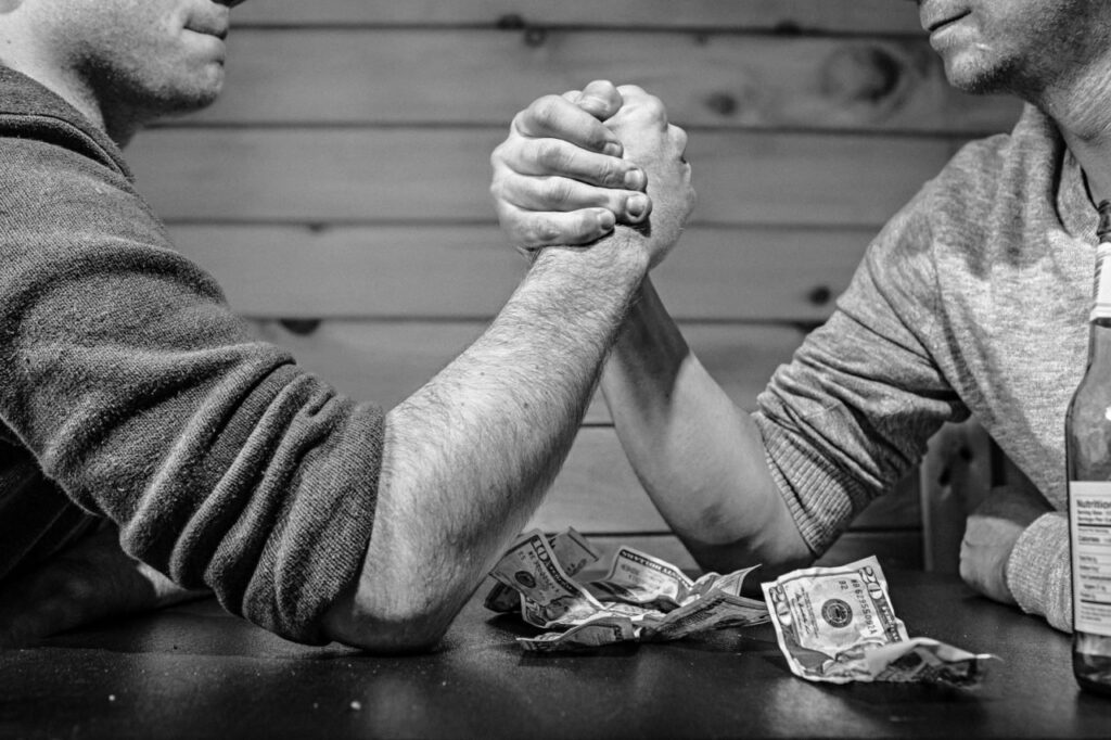 "Black and white image of two people arm wrestling over a table of money, symbolizing the concept of mutable versus immutable objects in Python programming."