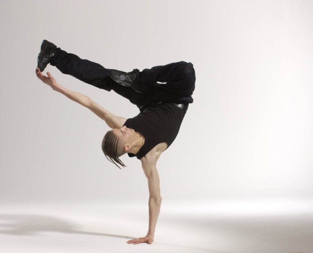 "Dancer performing an impressive one-handed handstand against a plain background, showcasing strength, flexibility, and artistic expression in breakdancing."