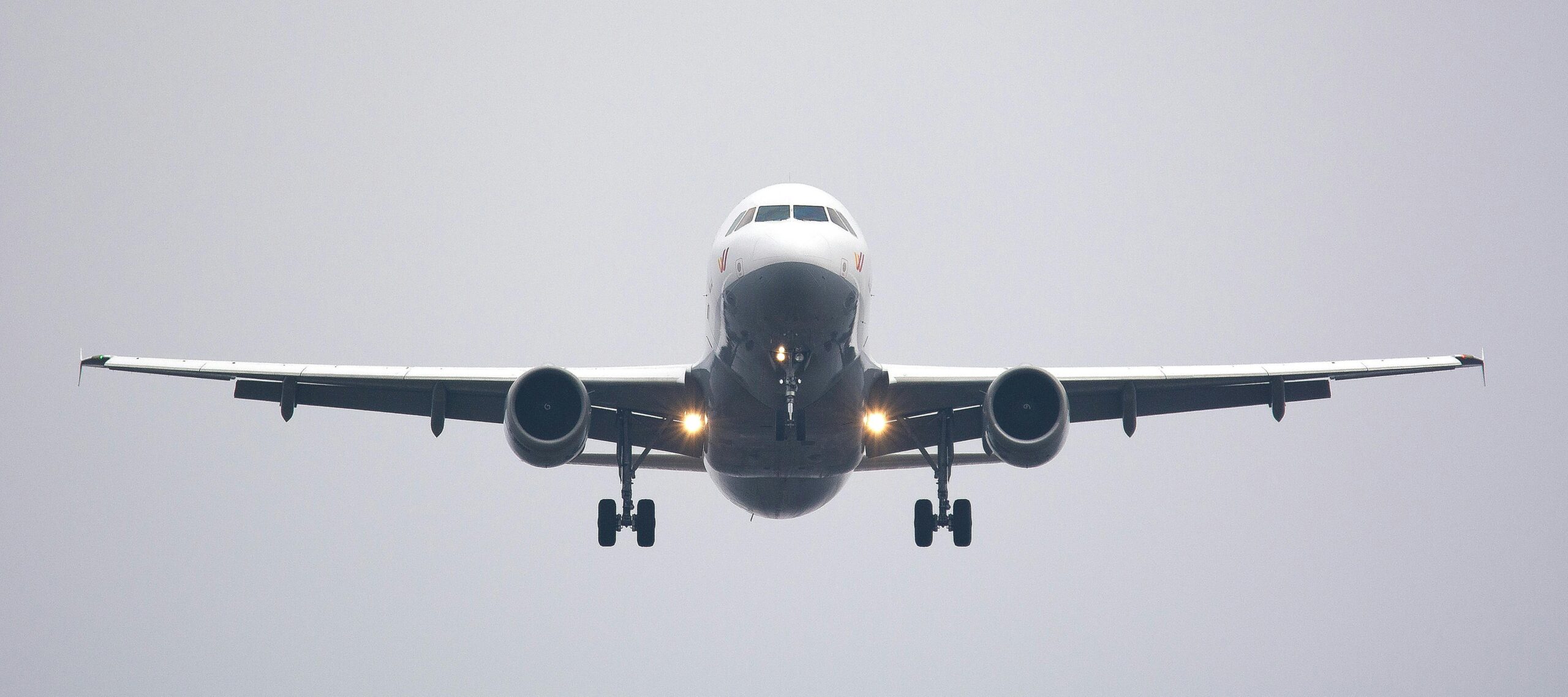 Front view of a commercial airplane approaching for landing with landing lights on against a cloudy sky