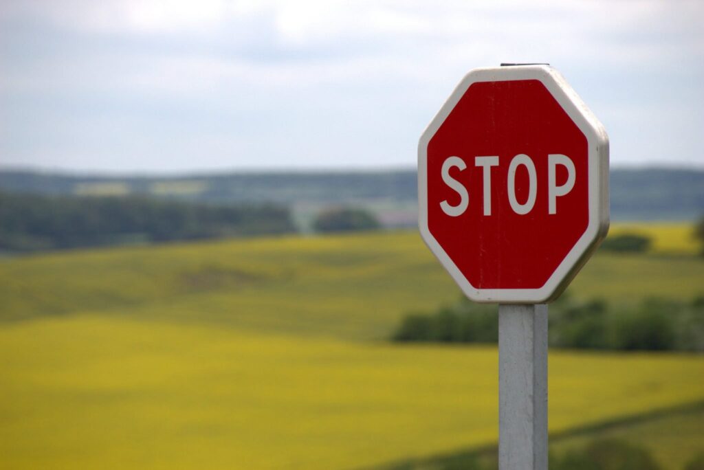 A red stop sign in a rural landscape with fields in the background, under a cloudy sky.